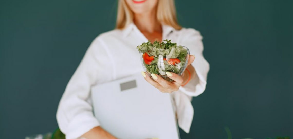 A woman with a vibrant smile offering a fresh salad bowl, promoting healthy eating.